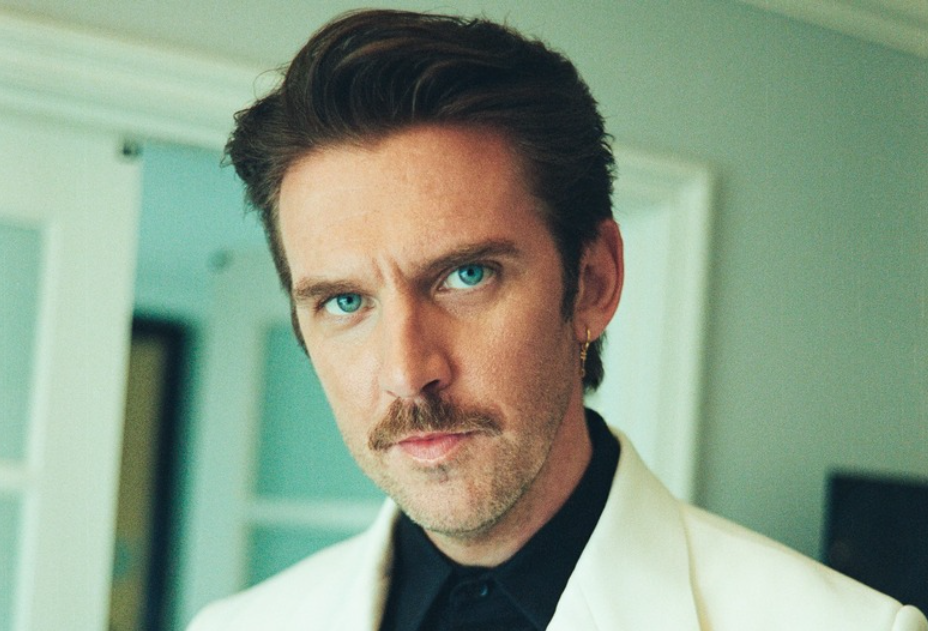 Dan Stevens wearing a white suit and looking toward the camera